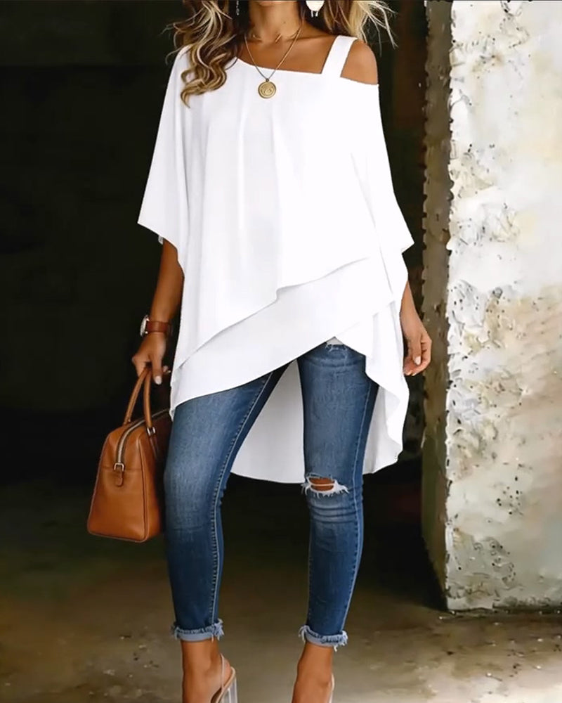 White asymmetrical blouse with off-shoulder straps paired with ripped jeans and brown handbag in rustic setting.