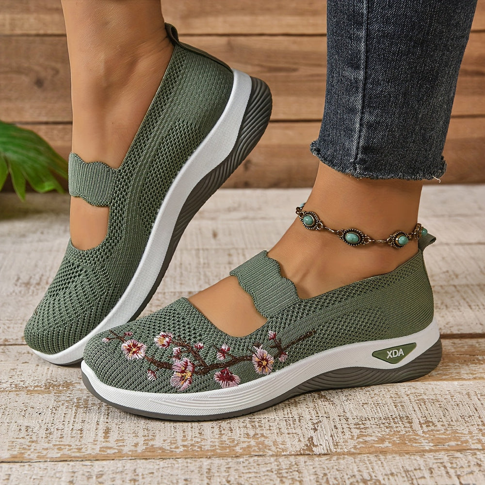 Side view of green orthopedic shoes with floral design, worn with jeans and anklet, on a wooden floor.