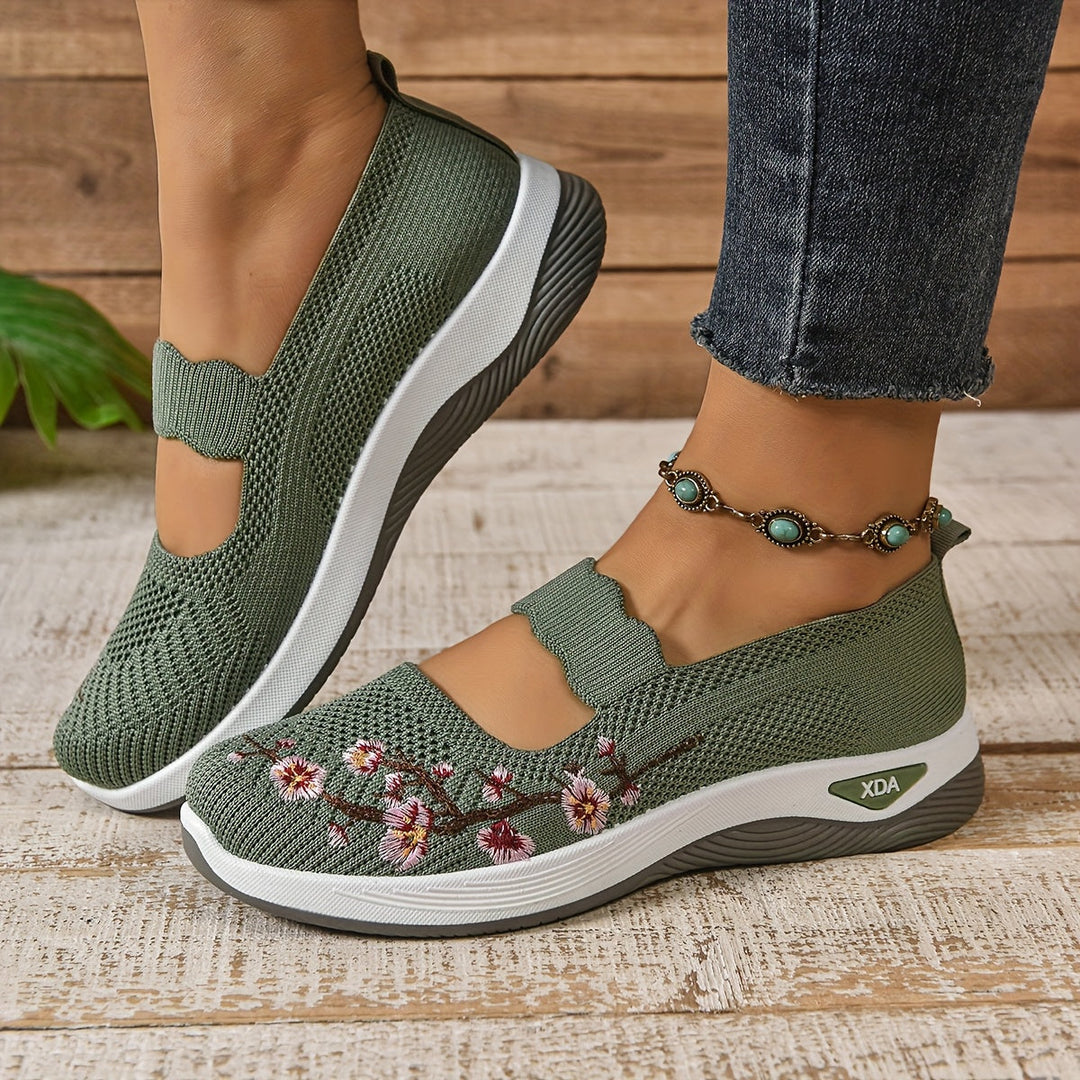 Side view of green orthopedic shoes with floral design, worn with jeans and anklet, on a wooden floor.