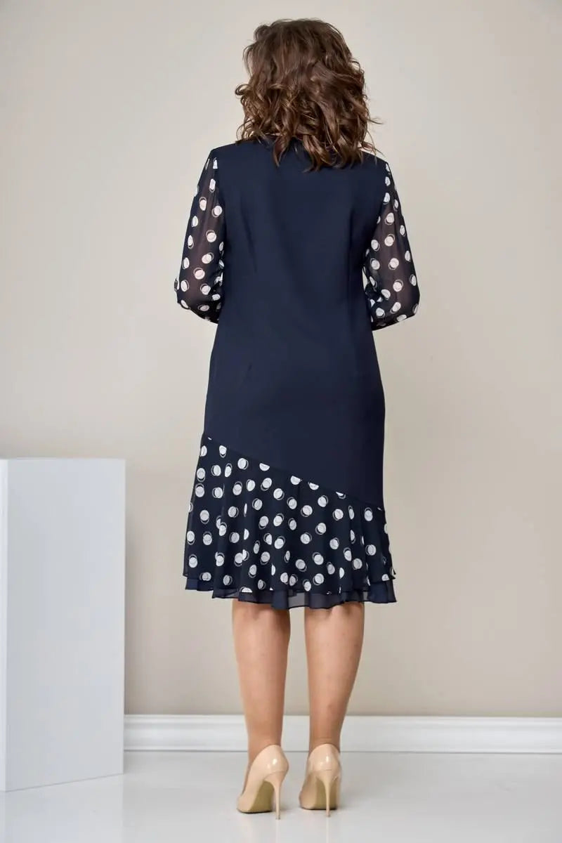 Back view of woman in navy dress with polka dot sleeves and ruffled hem, beige heels, in a minimalistic setting.