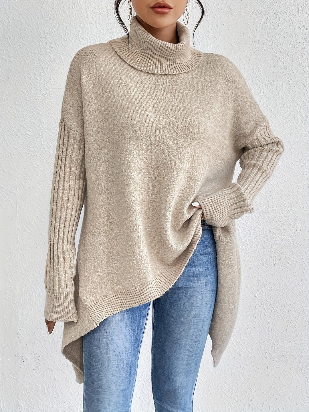 Beige sweater with turtleneck, long sleeves in ribbed texture, styled with jeans, against a white backdrop.