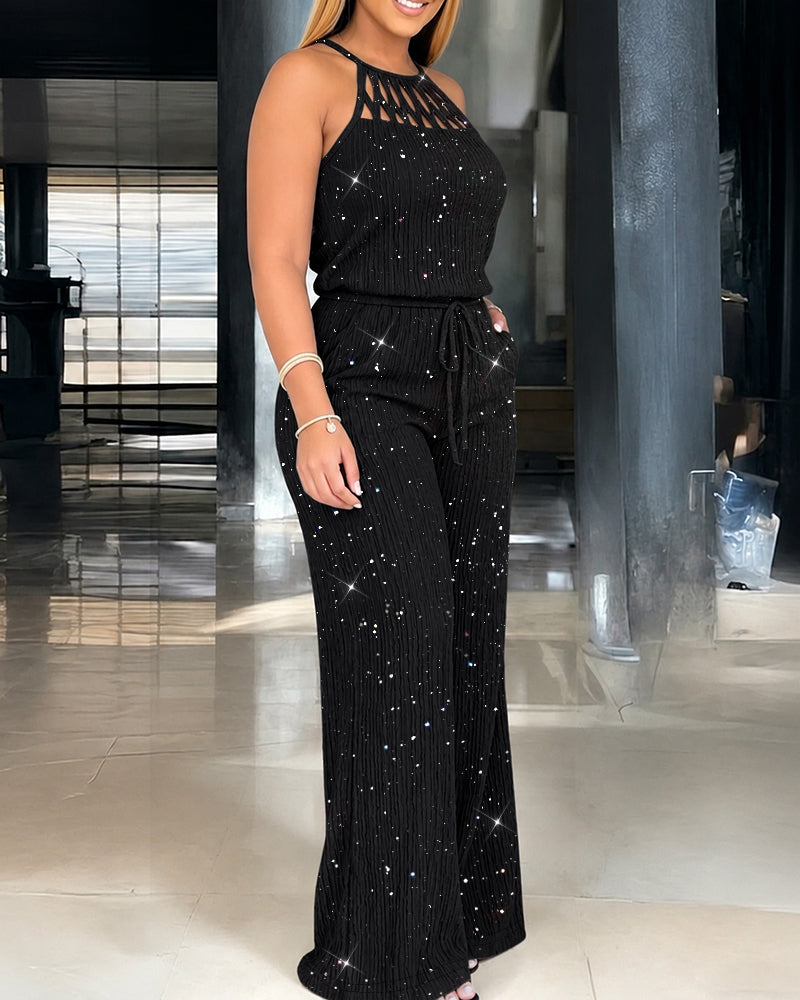 Side view of a model in a black glittery jumpsuit featuring a halter design. Indoor space with shiny flooring and columns.
