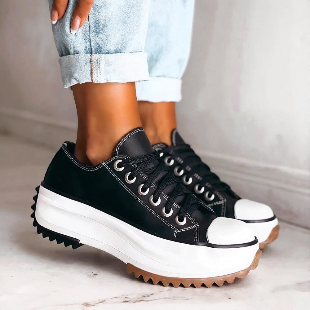 Black platform shoes with thick white soles and black laces, worn with light blue rolled-up jeans on a marble floor.