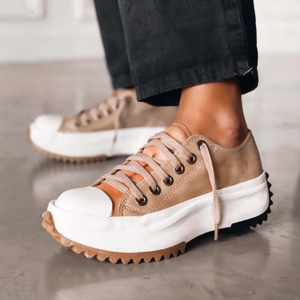 Tan platform shoes with thick white soles and tan laces, worn with black pants on a polished concrete floor.