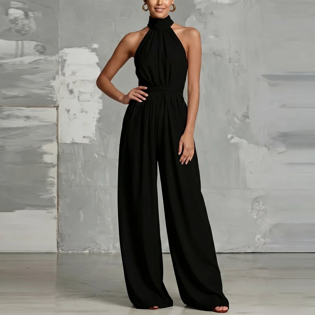 Black halter-neck jumpsuit with wide legs, hand on hip, in a minimalist studio.