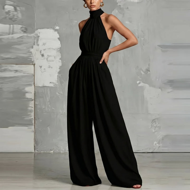 Stylish black halter-neck jumpsuit with flowing wide legs in a contemporary studio setting.