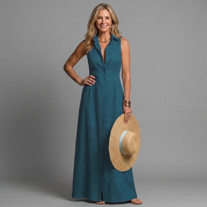 Woman in teal maxi shirt dress, holding a straw hat, in a studio setting.