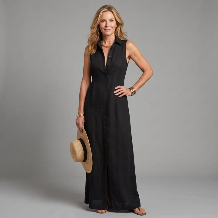 Woman in black maxi shirt dress, holding a straw hat, in a studio setting.