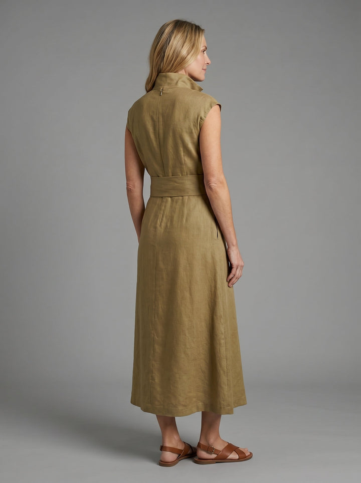 Back view of woman in khaki sleeveless dress with wide waistband, wearing sandals, posing in a studio with gray background.