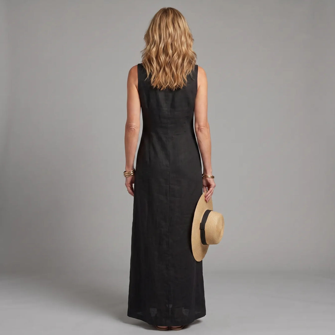 Back view of woman in black maxi shirt dress, holding a straw hat, in a studio setting.