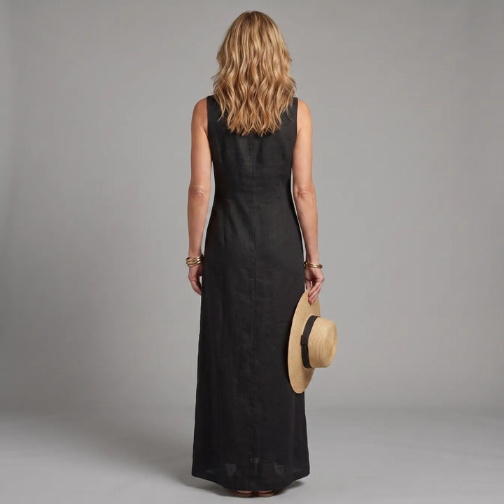 Back view of woman in black maxi shirt dress, holding a straw hat, in a studio setting.