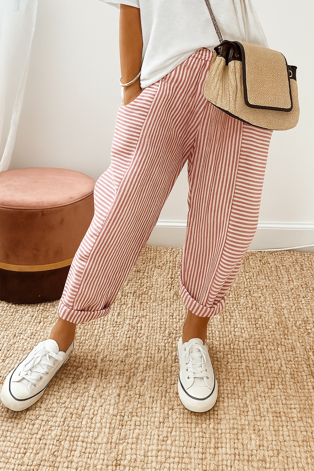 Person wearing red striped pants with white sneakers and a casual white top, standing on a textured beige carpet near a brown stool.