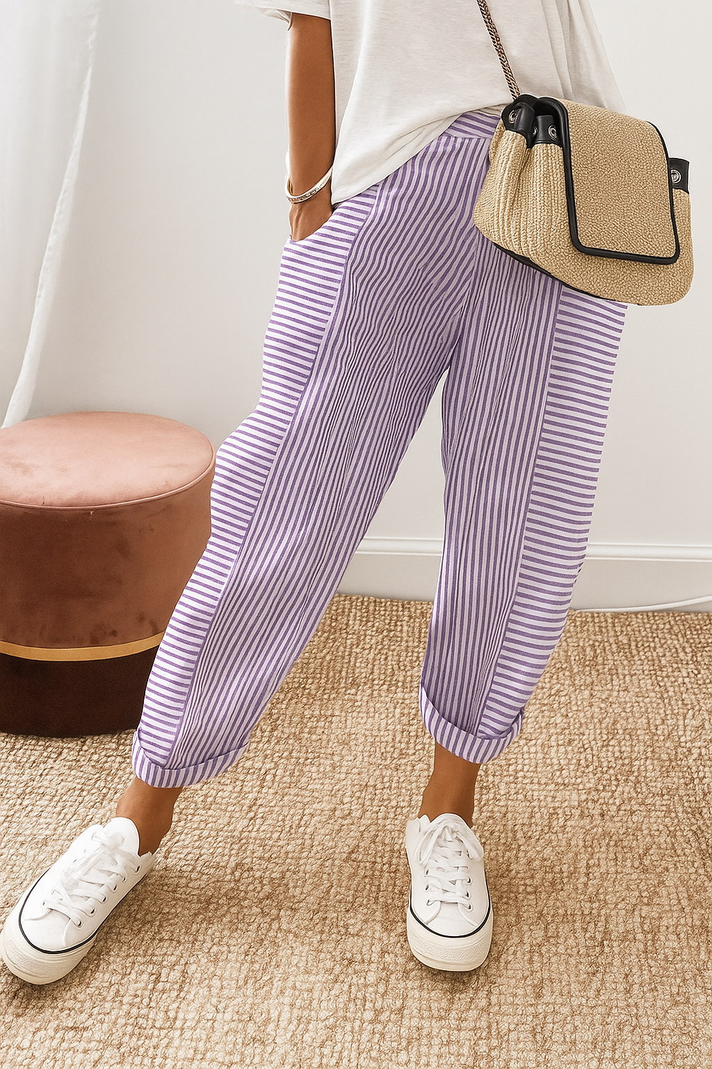 Person wearing purple striped pants with white sneakers and a casual white top, standing on a textured beige carpet near a brown stool.