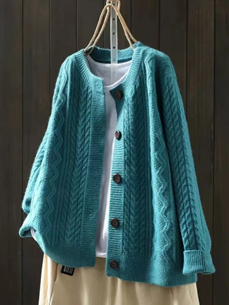 Teal knitted cardigan with button closure, layered over a white shirt, hanging against a dark wood background.