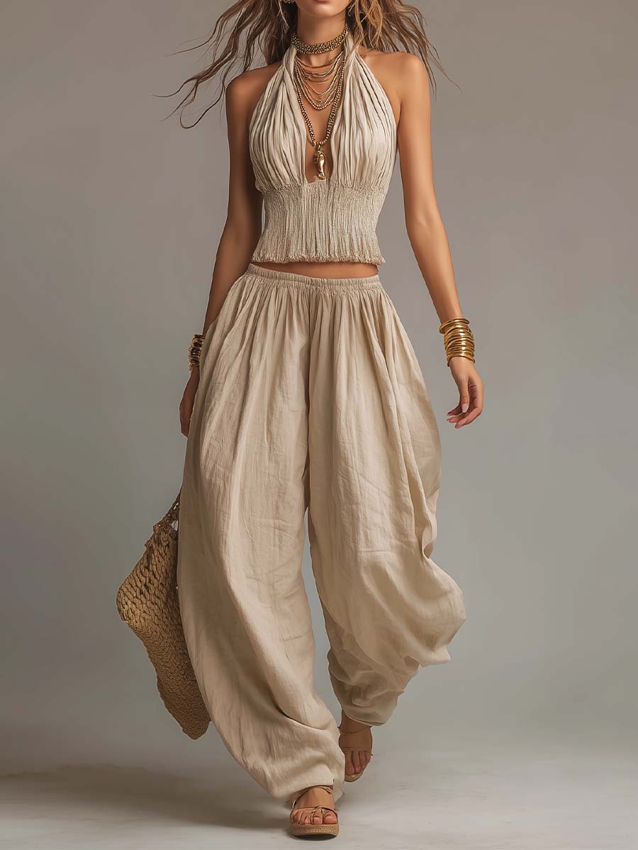 Beige two-piece set with a halter top and billowy pants, worn with jewelry and sandals. Studio background.