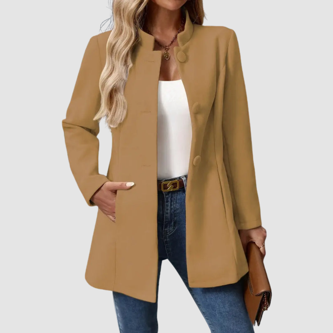 Brown jacket with large buttons, worn over white top and jeans, holding a clutch, plain background.