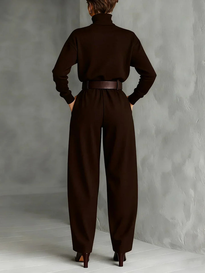 Back view of model wearing a brown top and straight-leg pants set with a belted waist in a gray studio.