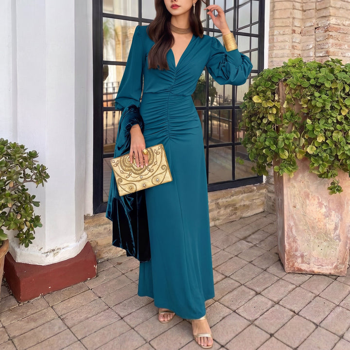 Stylish teal midi dress with ruched detailing and long sleeves, accessorized with gold accents, positioned on a tiled patio.