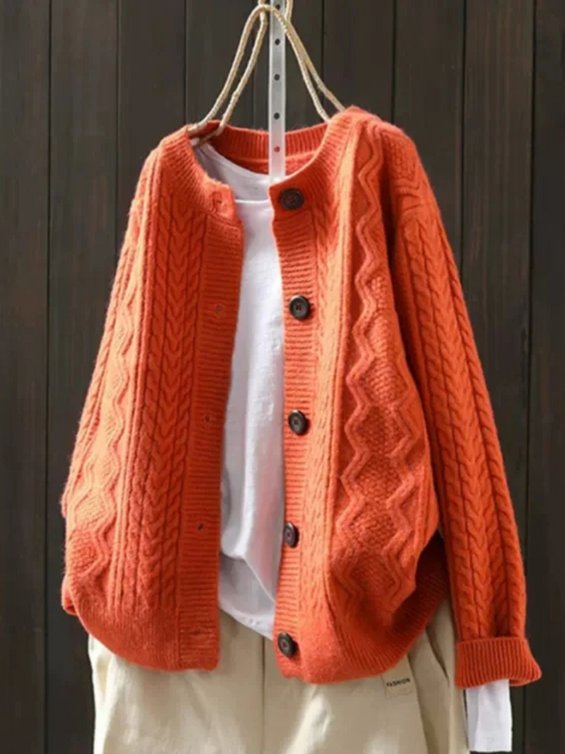 Orange knitted cardigan with button closure, layered over a white shirt, hanging against a dark wood background.