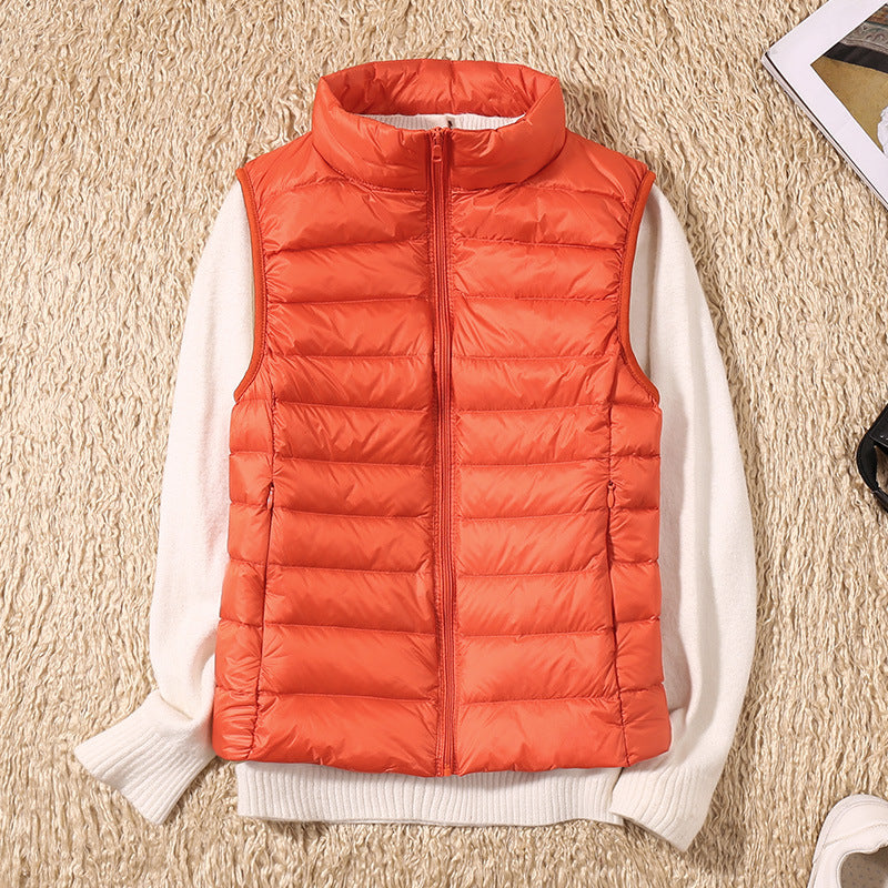 Orange puffer vest over a white sweater on a beige textured carpet, with accessories nearby.