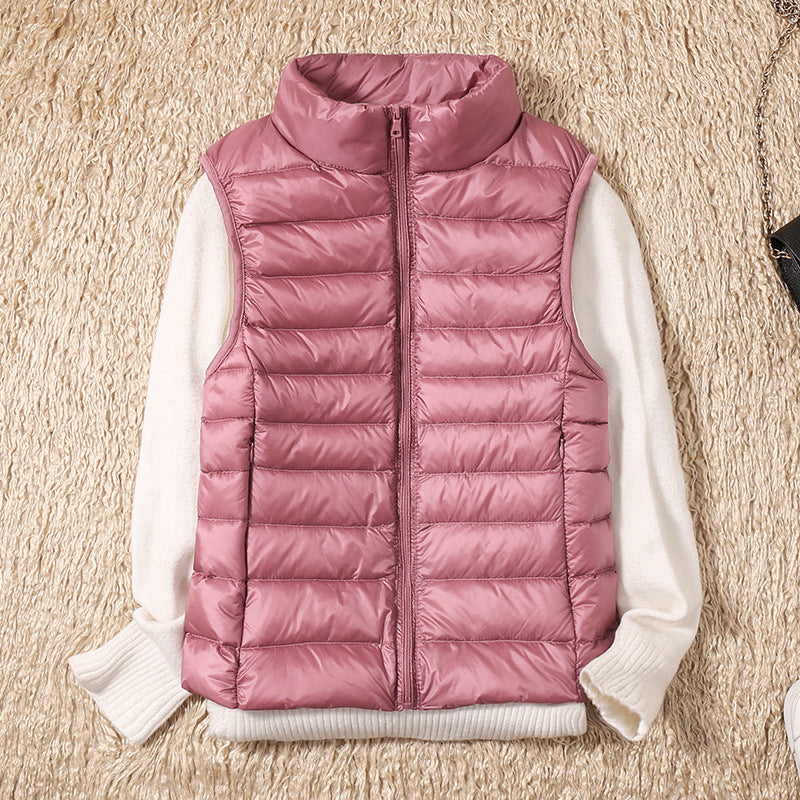 Pink puffer vest arranged over a white sweater on a beige textured background.