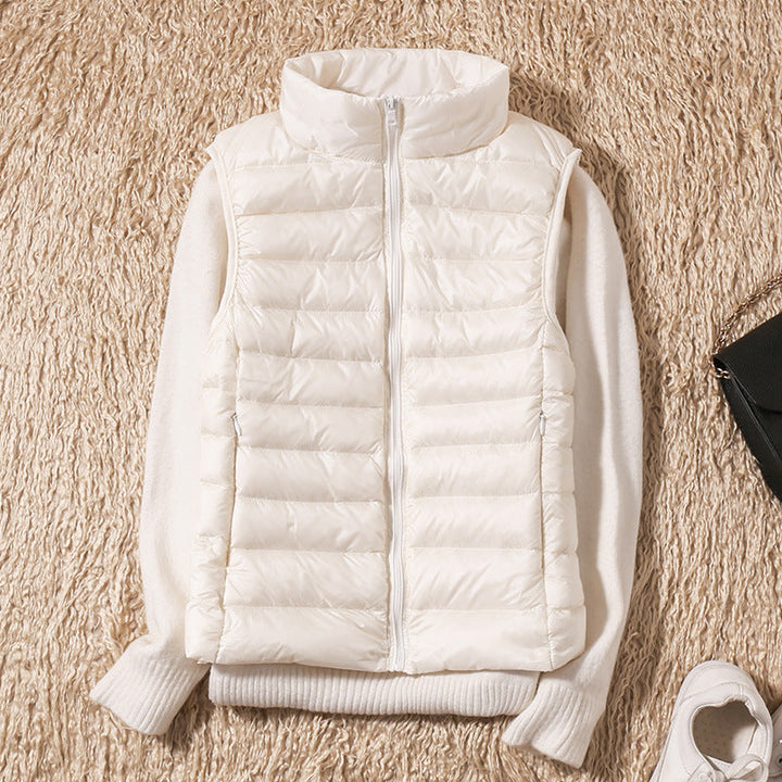White puffer vest over a white sweater on a beige textured surface with accessories.