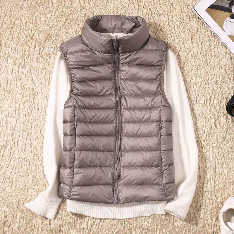 Grey puffer vest laid on a beige textured rug with a white sweater underneath beside accessories.