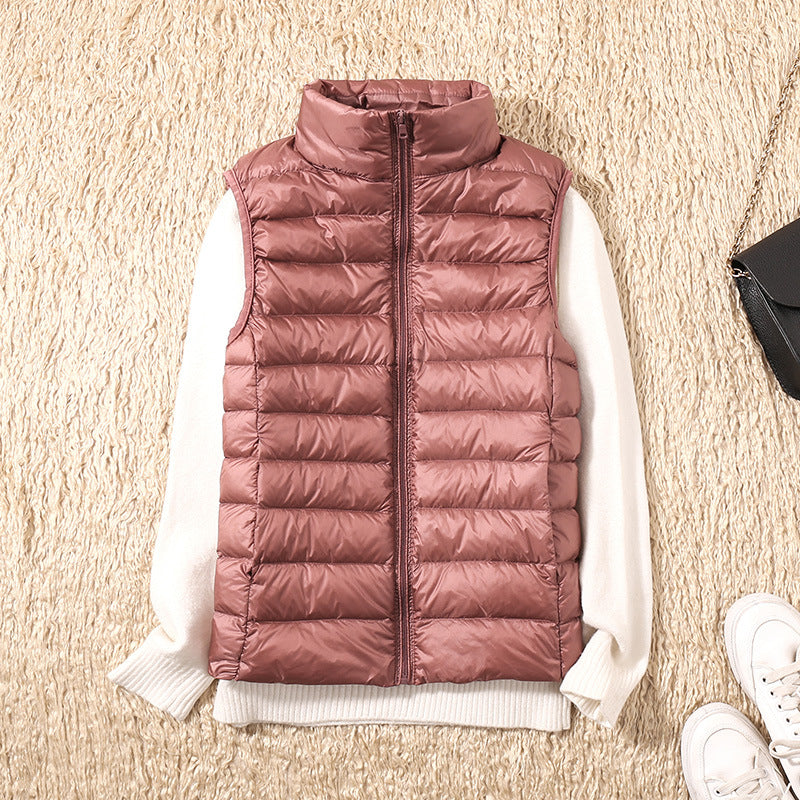 Dusty pink puffer vest laid out with a white sweater on a textured beige rug.