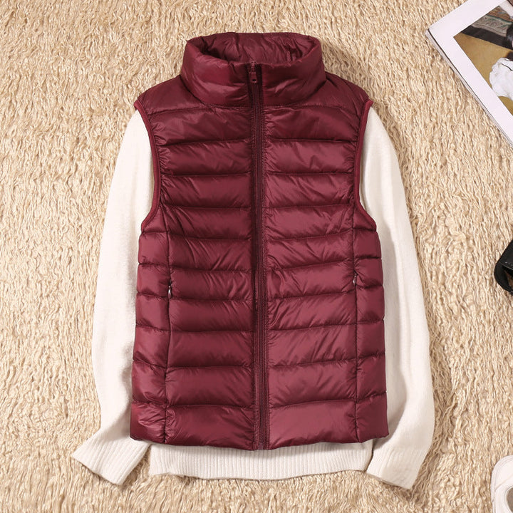 Maroon puffer vest on a beige carpet with a white sweater underneath, surrounded by accessories.