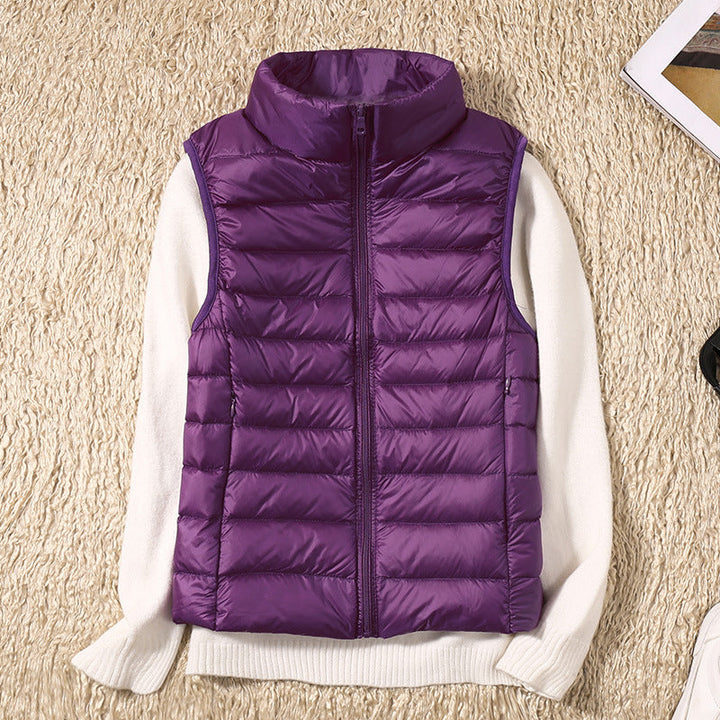 Purple puffer vest on a beige rug with a white sweater, next to accessories.