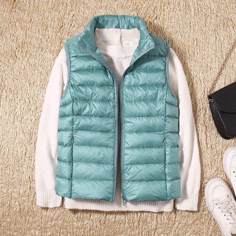 Aqua puffer vest on a beige textured background with a white sweater beneath.