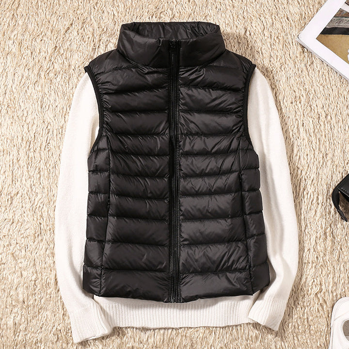 Black puffer vest displayed on a beige textured surface with a white sweater beneath.