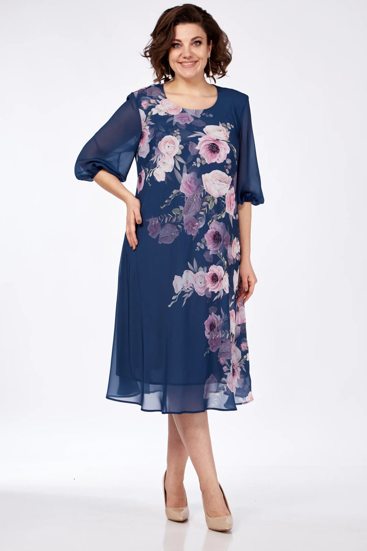 Woman in a navy floral dress with flowing sleeves, posed in a studio with a white background.