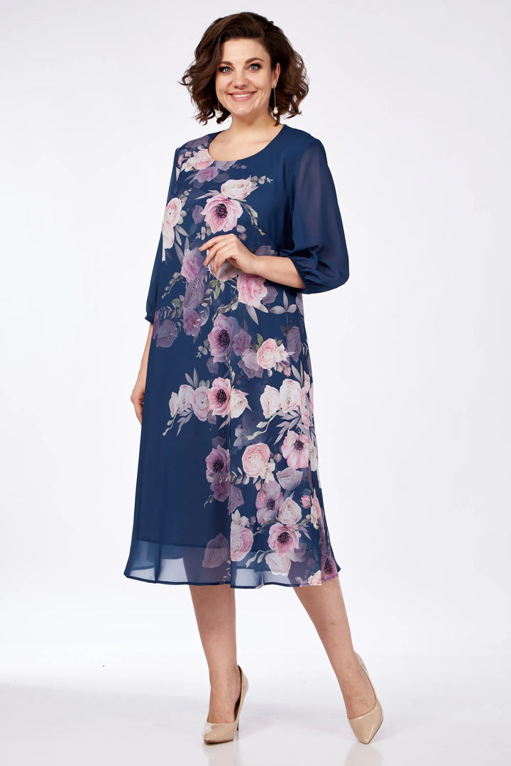Woman in navy floral dress with elegant flowery print, posed in a studio with a white background.
