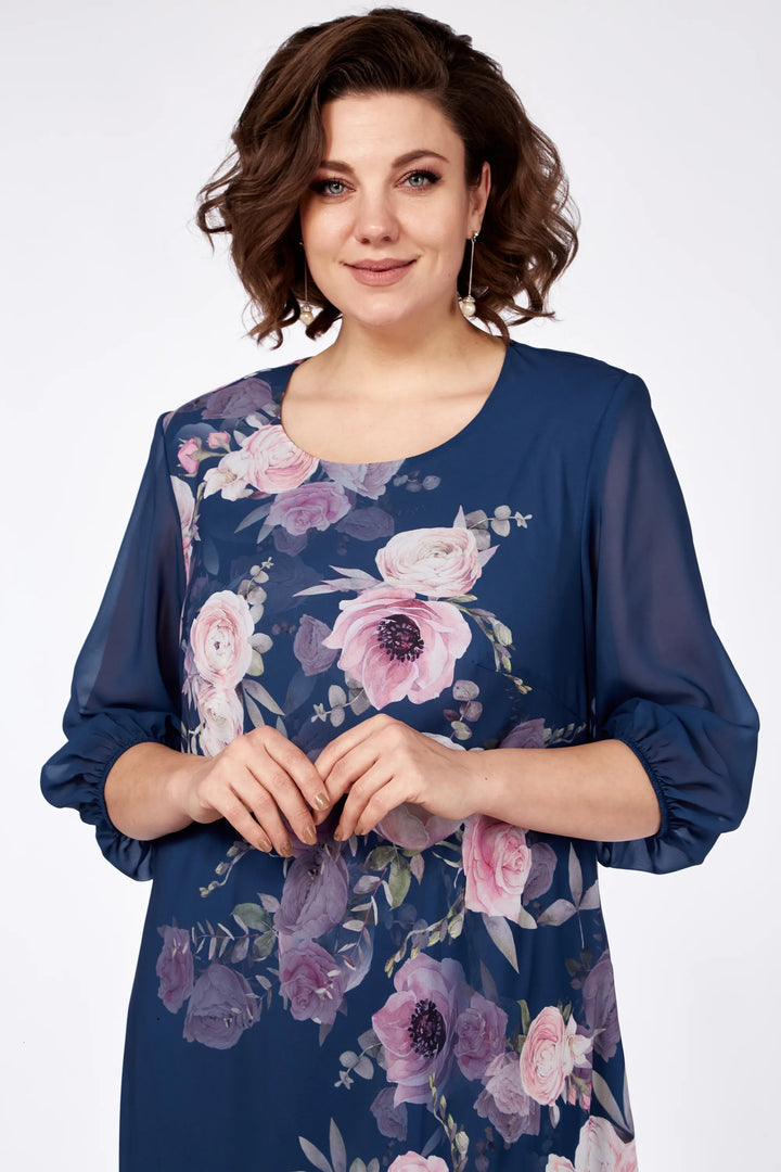 Close-up of a woman in a navy floral dress with vibrant flowers, posed against a white background.