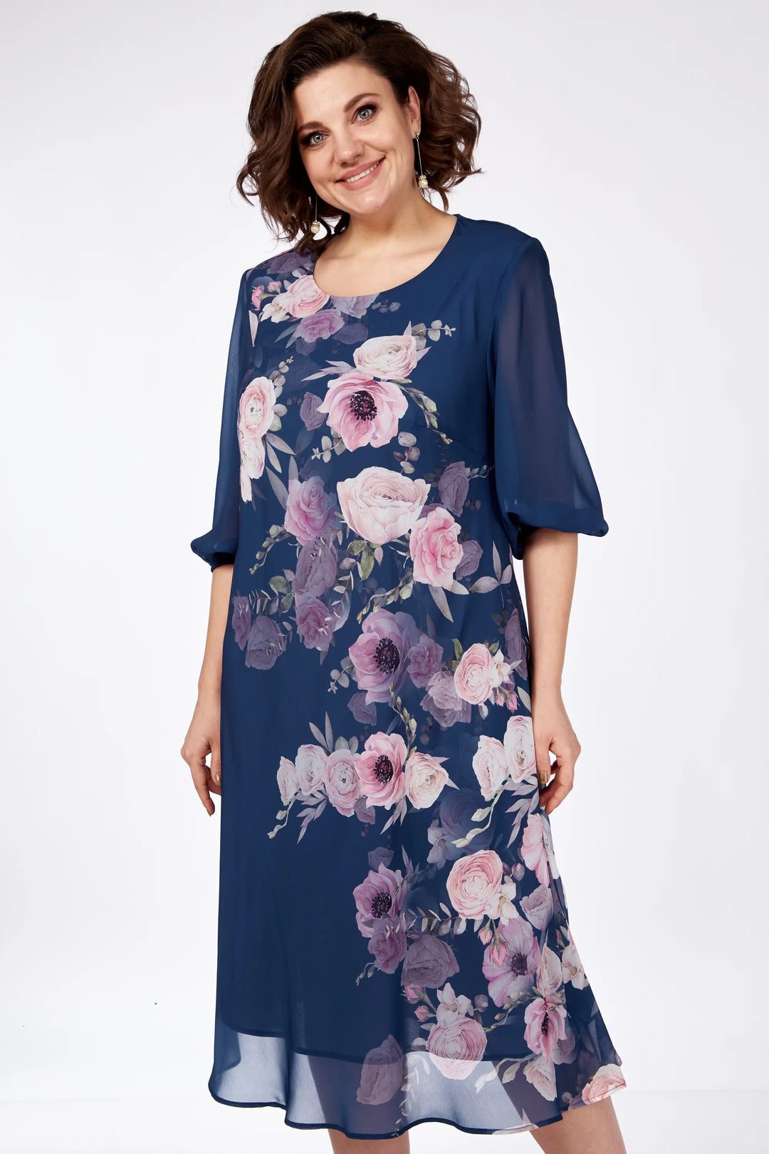 Model wearing navy floral dress with pink and purple flowers, standing in a white studio setting.