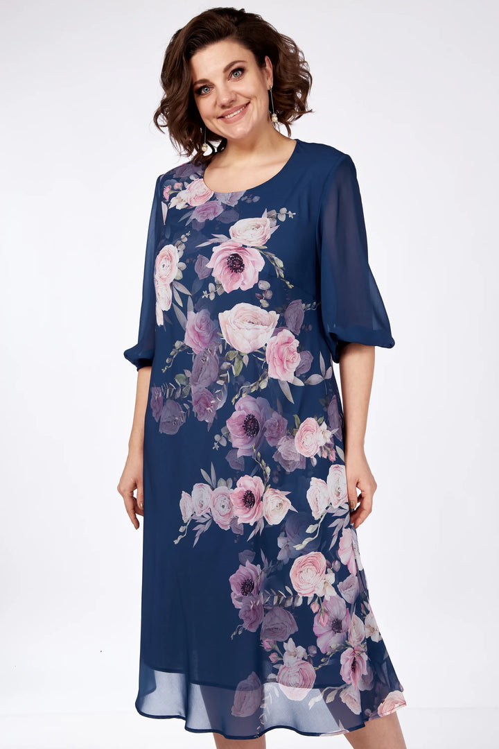 Model wearing navy floral dress with pink and purple flowers, standing in a white studio setting.