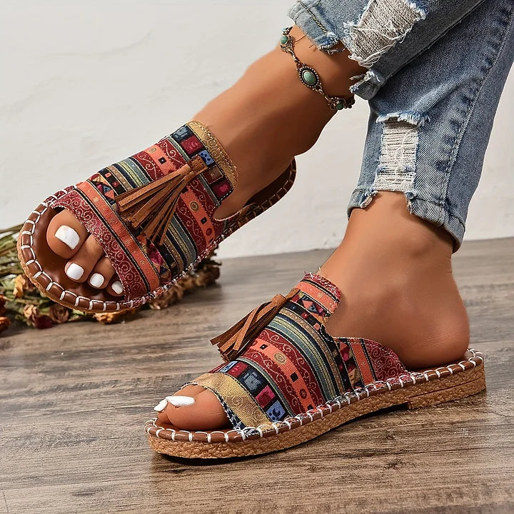Side view of colorful orthopedic sandals with tassels worn on wooden floor indoors.