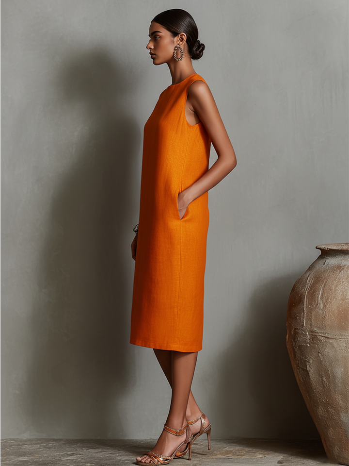 Side profile of orange midi dress with pockets, sleeveless, model standing in studio with pottery.