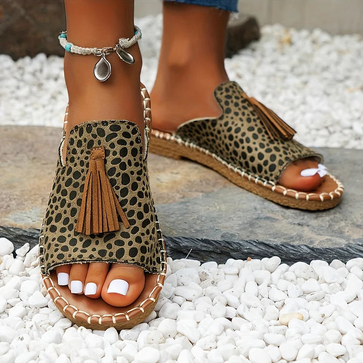 Close-up of polka dot orthopedic sandals with tassels worn outdoors on stone path.