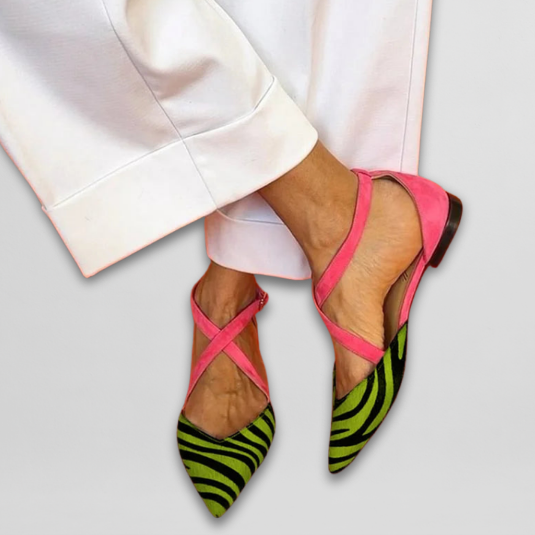 Pink ballet flats with green zebra pattern, shown with white pants on a light gray background.
