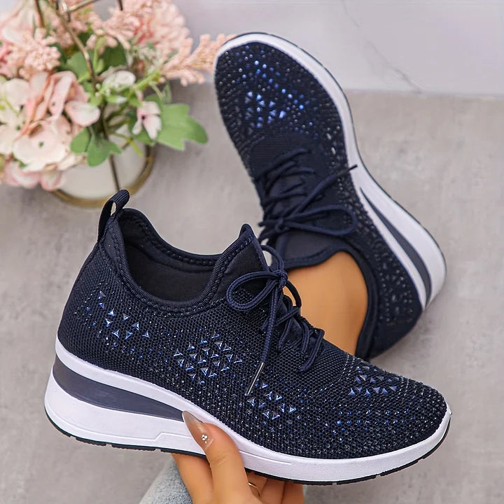 Navy blue orthopedic sneakers with a sparkling design, displayed in a soft-lit room with floral decor.