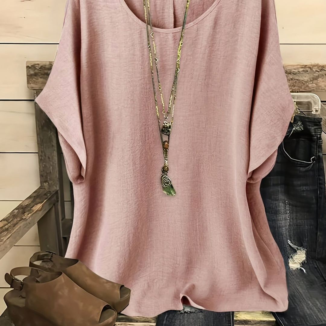 Blush pink loose summer top on hanger with necklace, sandals, and jeans on rustic bench.