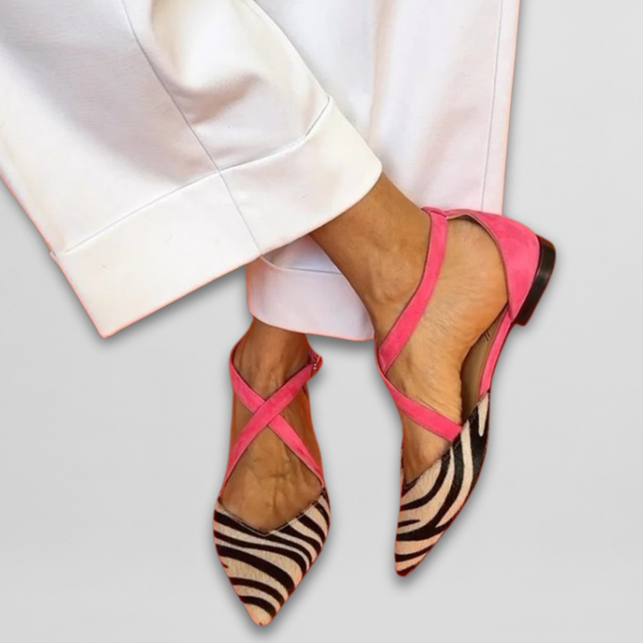 Pink ballet flats with zebra pattern and straps, paired with white pants on a light gray background.