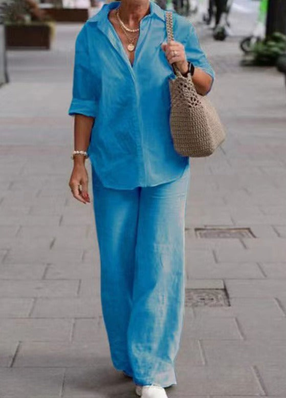 Woman wearing a bright blue two-piece set with rolled cuffs, strolling with a beige woven bag on a city sidewalk.
