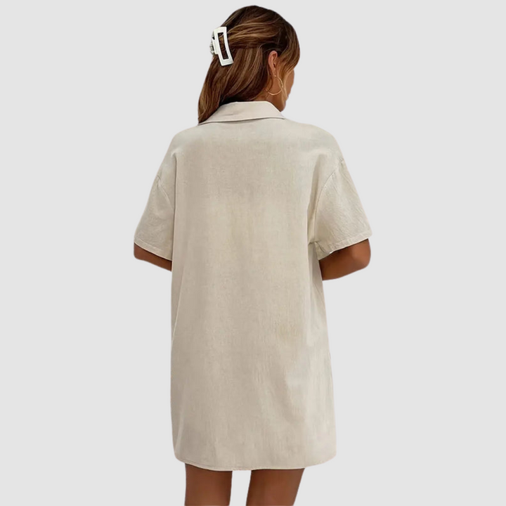 Back view of woman in beige button-up dress, hair clipped, against a studio background.