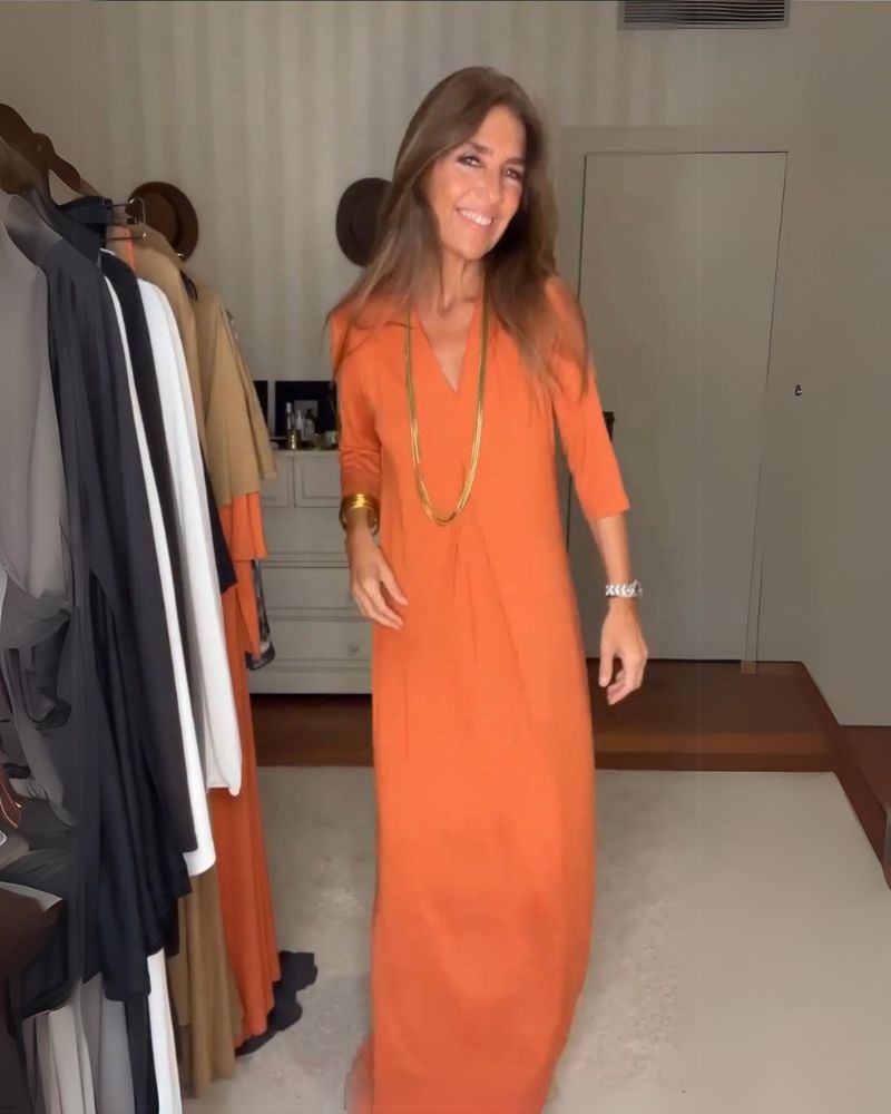 Person wearing an orange casual maxi dress with long sleeves, in a room with hanging clothes.