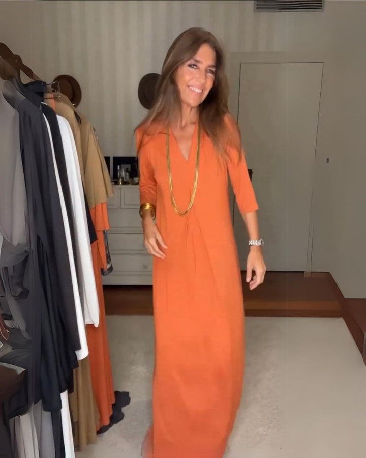 Person wearing an orange casual maxi dress with long sleeves, in a room with hanging clothes.