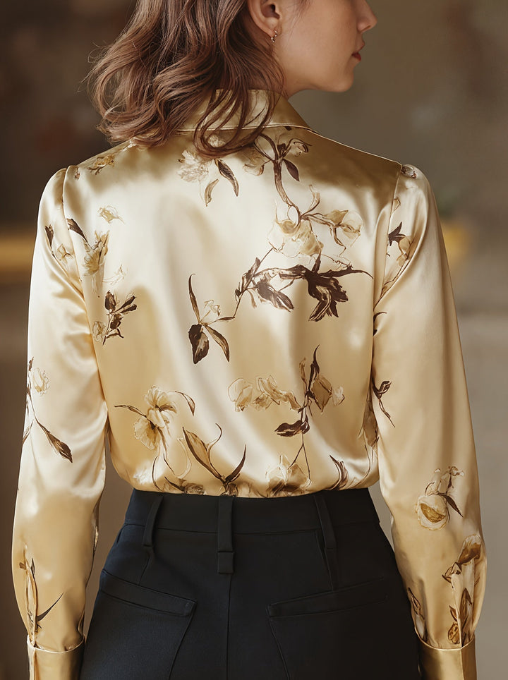 Back of gold satin blouse with floral design, model posing indoors in a refined environment.