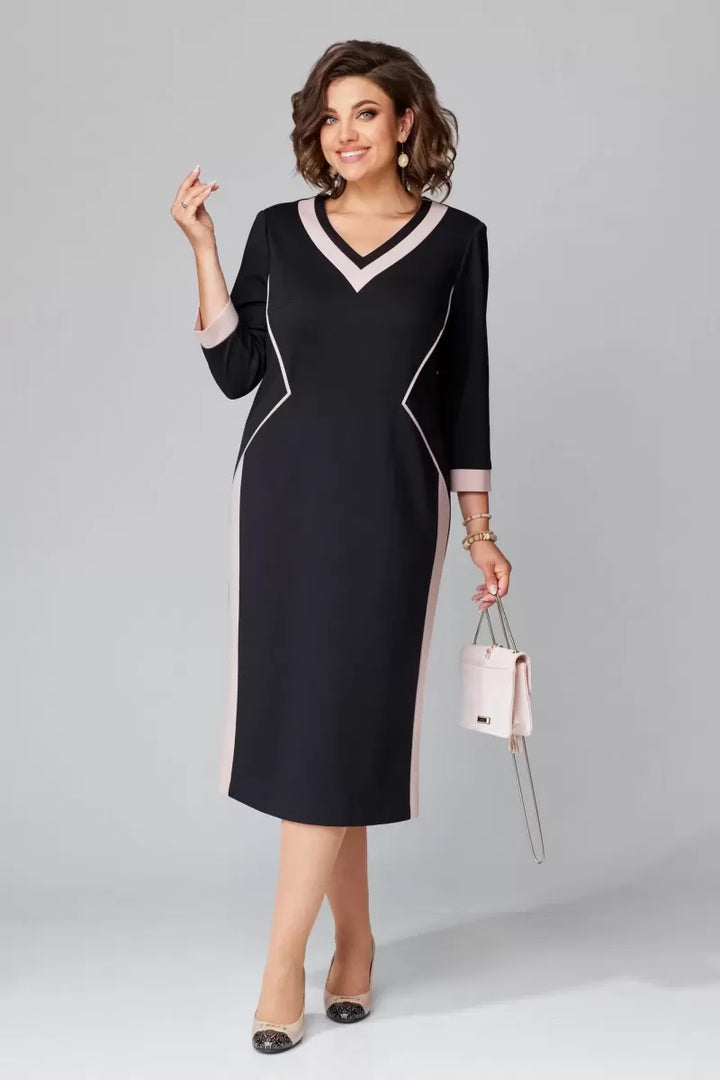 Model smiling in black V-neck dress with pink accents, holding a handbag in a studio environment.